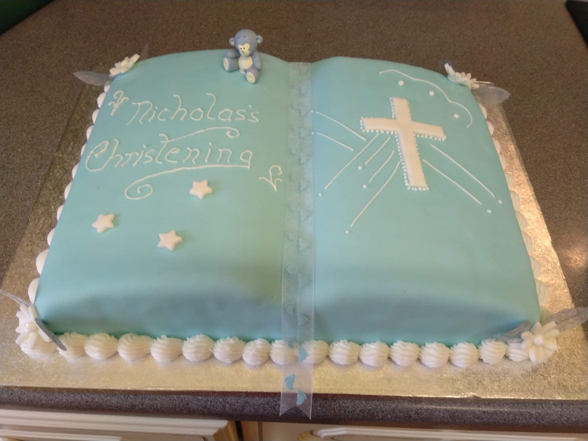 A christening cake iced as an open book with a teddy bear and piped lettering
