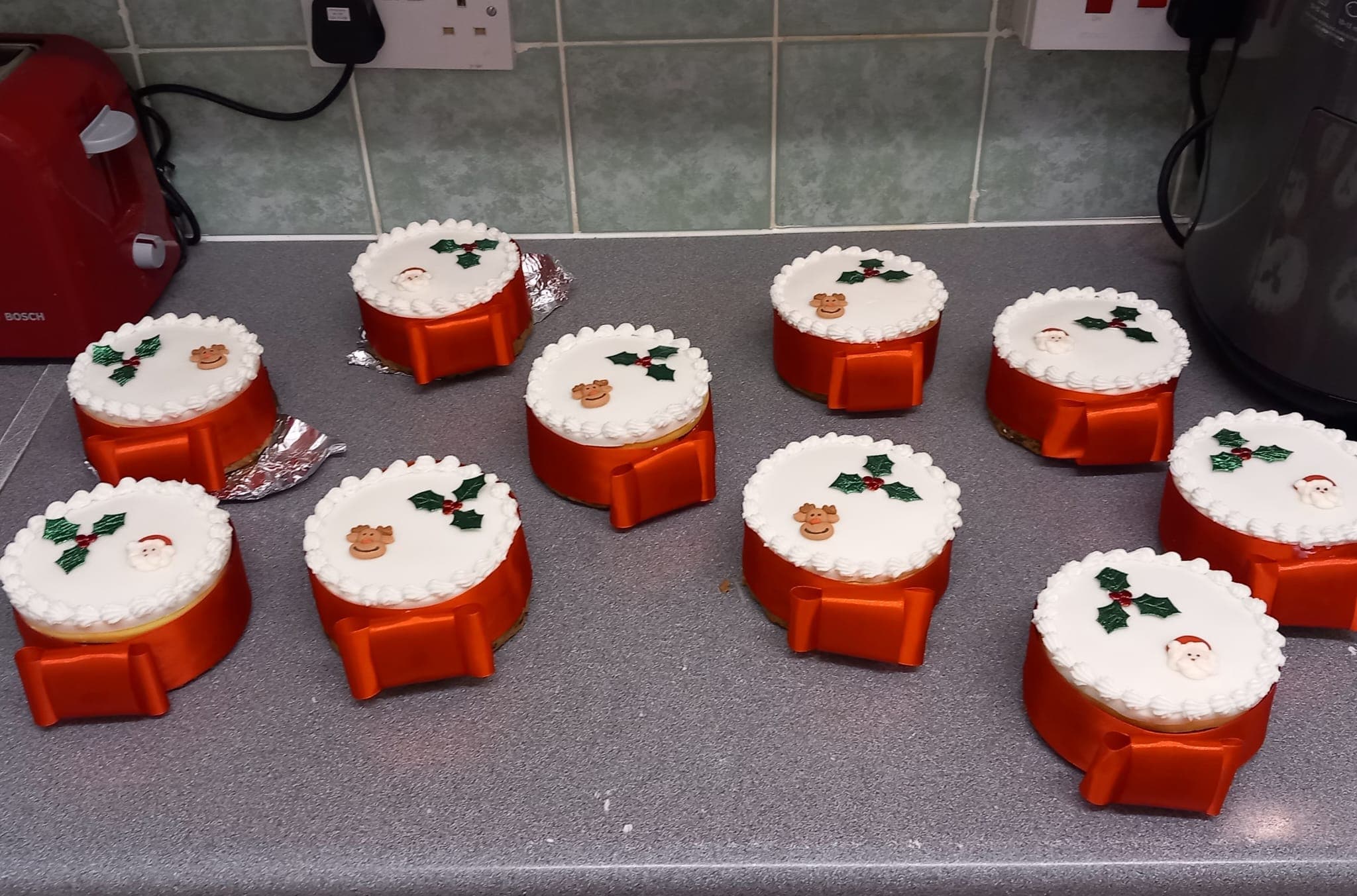 Ten small iced Christmas cakes finished with red ribbon, holly and piped borders