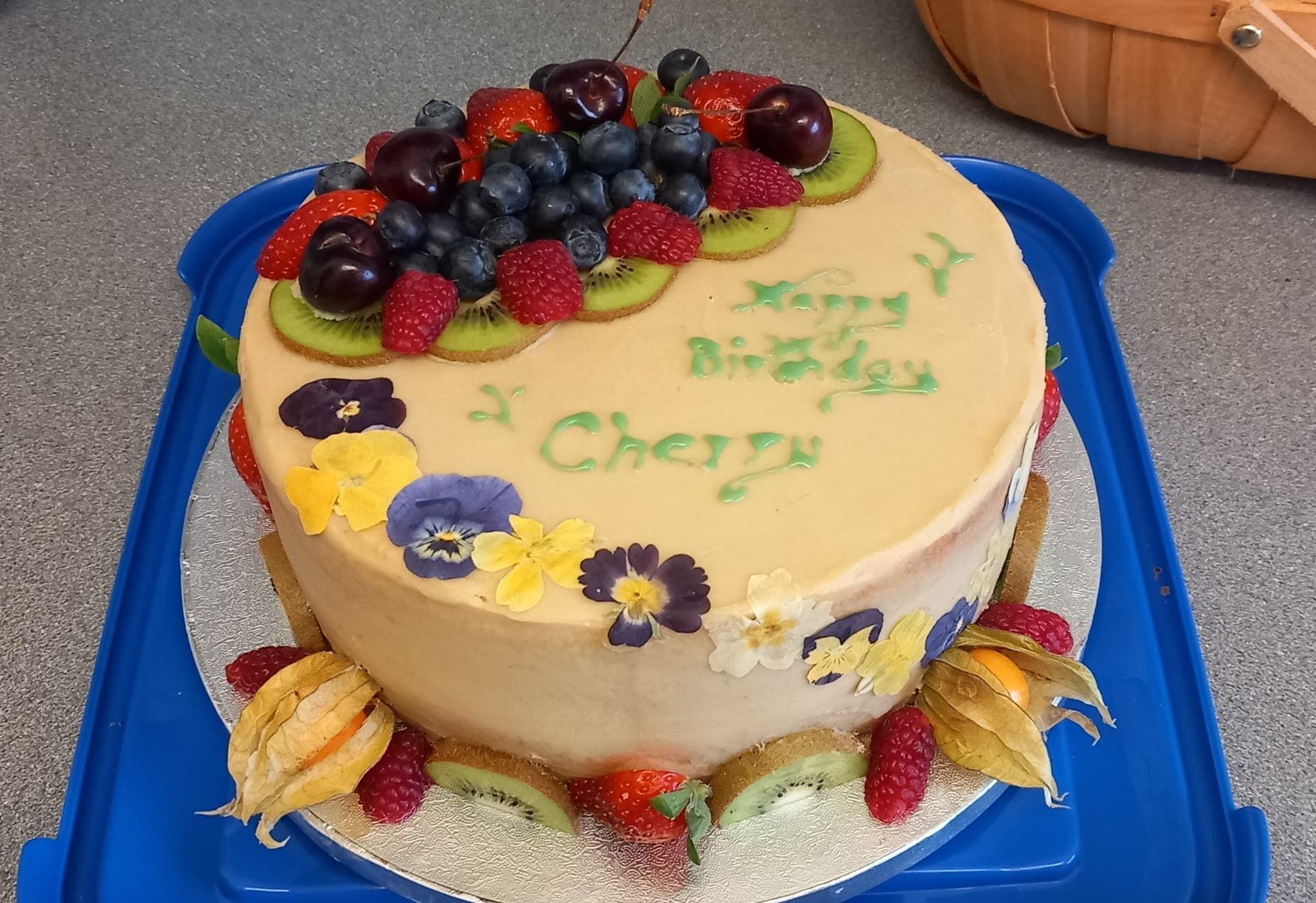 A birthday cake topped with fresh fruit and decorated with edible flowers