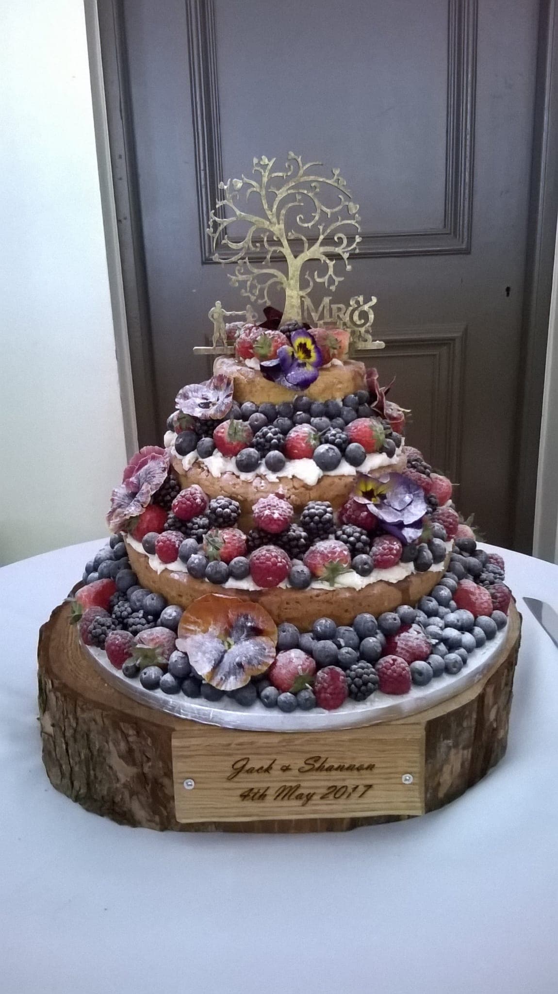 A three-tier wedding sponge piled with fresh berries and sugared flowers on a rustic log stand